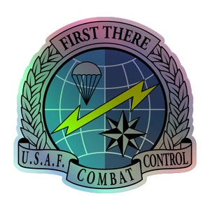 Może przedstawiać: Okrągły emblemat w kolorze niebieskim i zielonym z globem, błyskawicą, kompasem i spadochronem. Wokół emblematu widnieje tekst "FIRST THERE U.S.A.F. COMBAT CONTROL".