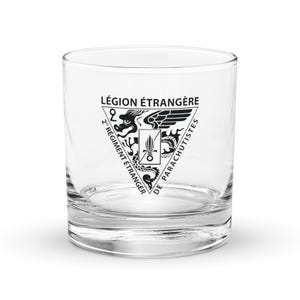 Puede incluir: Un vaso bajo transparente con un emblema en blanco y negro. El emblema presenta el texto "LÉGION ÉTRANGÈRE" y "2° RÉGIMENT ÉTRANGER DE PARACHUTISTES" que rodea un dragón y otros símbolos. El vaso es cilíndrico con una base gruesa.