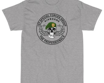 Puede incluir: Camiseta gris con un gráfico en blanco y negro de una calavera con un gorro verde con un emblema dorado. El gráfico está rodeado por un círculo con el texto "1st Special Forces Group Airborne The Professionals".