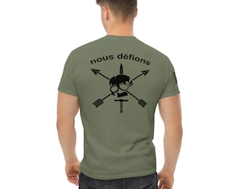 Puede incluir: Una camiseta verde con un diseño de calavera y huesos cruzados negros. El texto "nous défions" está por encima de la calavera.
