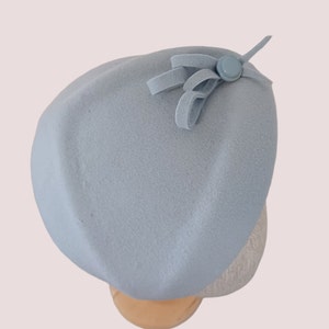 Pu&ograve; includere: Un basco azzurro chiaro con un piccolo fiocco e un dettaglio a bottone. Il cappello &egrave; realizzato in un materiale morbido ed &egrave; esposto su una testa di manichino. Il basco &egrave; uno stile classico, adatto a varie occasioni.