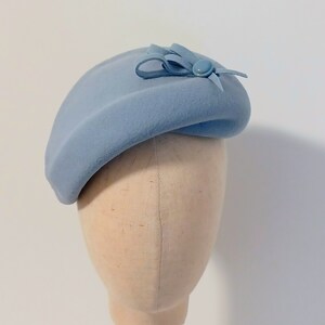 Pu&ograve; includere: Un cappello a forma di basco azzurro chiaro con un piccolo fiocco e un dettaglio a bottone. Il cappello &egrave; realizzato in un materiale morbido ed &egrave; esposto su una testa di manichino. Il cappello &egrave; di colore pieno e ha un design classico ed elegante.
