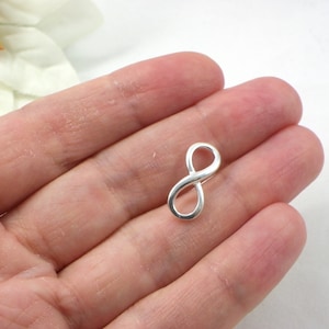 Könnte beinhalten: Ein silberner Anhänger in Form eines Unendlichkeitszeichens.