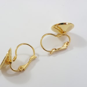 Peut inclure: Deux apprêts de boucles d'oreilles à clip dorés. Chaque apprêt comporte un disque rond et plat et une fermeture à charnière à levier. Les boucles d'oreilles sont conçues pour être fixées au lobe de l'oreille sans perçage.