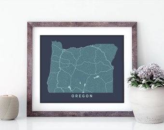 May include: A framed print of a map of Oregon with a dark blue background and light blue lines representing roads. The state name "OREGON" is printed in white at the bottom of the map.