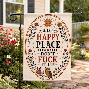 Puede incluir: Una bandera de jardín beige con un diseño ovalado que presenta el texto "THIS IS OUR HAPPY PLACE DON'T FUCK IT UP". El diseño incluye un sol, flores, hojas y un búho. La bandera está colgada afuera en un jardín.