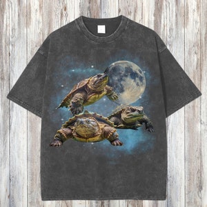 Könnte beinhalten: Ein dunkelgraues T-Shirt mit Vintage-Waschung, auf dem drei Schildkröten vor einem Vollmond und Sternen fliegen.