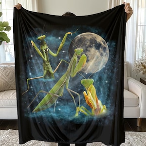 May include: Black blanket featuring a vibrant illustration of three praying mantises against a backdrop of a full moon and a starry night sky. The mantises are depicted in shades of green and yellow.