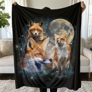 May include: A black fleece blanket with a design of three red foxes in a starry night sky with a full moon.