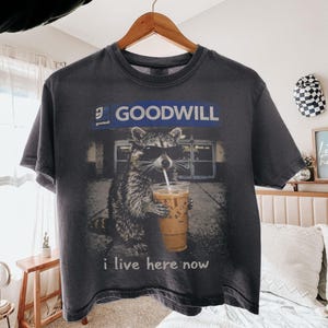 Shirt wasbeer tweedehands, ik woon hier nu grappig spaarzaam shirt, shirt goodwill humor, grafisch T-shirt wasbeer ijskoffie, kringloopwinkel minnaar cadeau