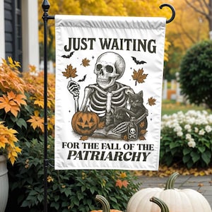 May include: A white garden flag with the text "JUST WAITING FOR THE FALL OF THE PATRIARCHY" features a skeleton, black cat, and jack-o'-lantern. The flag is displayed outdoors with pumpkins and fall foliage.