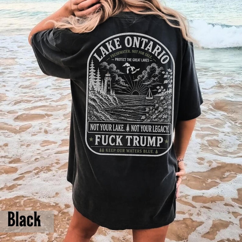May include: A black short-sleeve t-shirt featuring a white graphic on the back. The design depicts a lighthouse, trees, and a sailboat on Lake Ontario with the text: LAKE ONTARIO, PROTECT THE GREAT LAKES, NOT YOUR LAKE. NOT YOUR LEGACY. FUCK TRUMP.