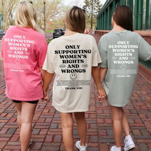 May include: Three people wearing t-shirts with the text "Only Supporting Women's Rights and Wrongs" printed on the back. The shirts are in pink, beige, and green.