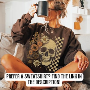 May include: Brown sweatshirt with a skull and floral graphic design. The design includes a skull, daisies, and a checkered pattern. The text at the bottom of the image reads: PREFER A SWEATSHIRT? FIND THE LINK IN THE DESCRIPTION!