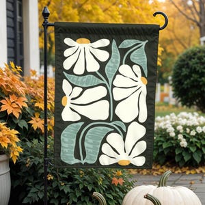 Puede incluir: Una bandera de jardín con fondo negro y un diseño floral blanco. Las flores son estilizadas y tienen un estilo retro. La bandera tiene un mensaje de bienvenida verde y blanco.