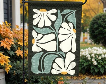 May include: A garden flag with a black background and a white floral design. The flowers are stylized and have a retro feel. The flag has a green and white welcome message.