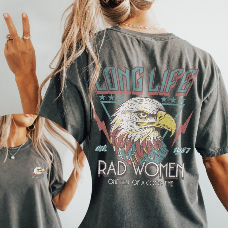 Op de afbeelding: Een donkergrijs T-shirt met een grafische print van een adelaar met de tekst "Long Life est. 1987 Rad Women One Hell of a Good Time" op de achterkant.