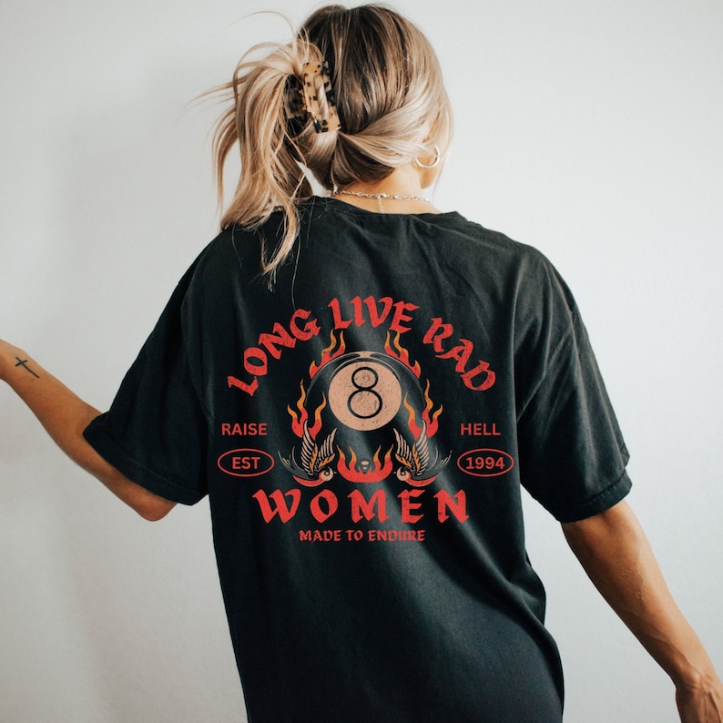 May include: Black t-shirt with a red and white graphic print of a flaming eight ball with the text "Long Live Rad" above and "Women Made to Endure" below. The graphic also includes the text "Raise Est 1994 Hell" in a circle.