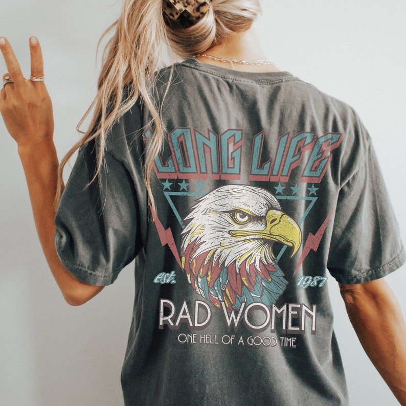 Op de afbeelding: Een donkergrijs T-shirt met een vintage-stijl afbeelding van een adelaar met de tekst "Long Life Est. 1987 Rad Women One Hell Of A Good Time".