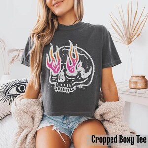 May include: Dark gray cropped boxy tee featuring a white skull graphic with pink and orange flames. The t-shirt has a crew neck and short sleeves. The text "Cropped Boxy Tee" is at the bottom of the image.