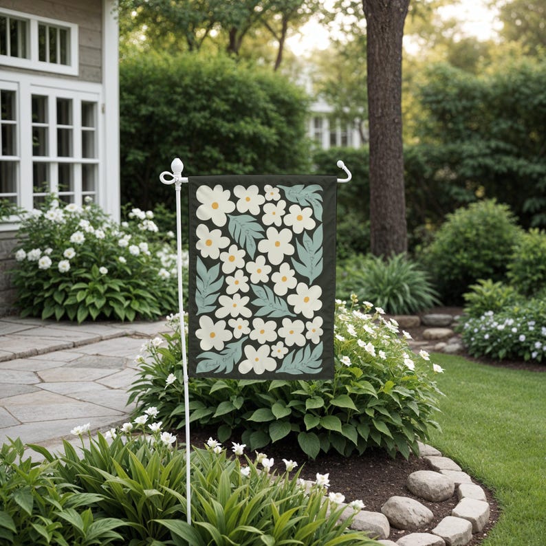 May include: A garden flag with a white floral pattern on a dark green background. The flag is hanging on a white pole in a garden setting.