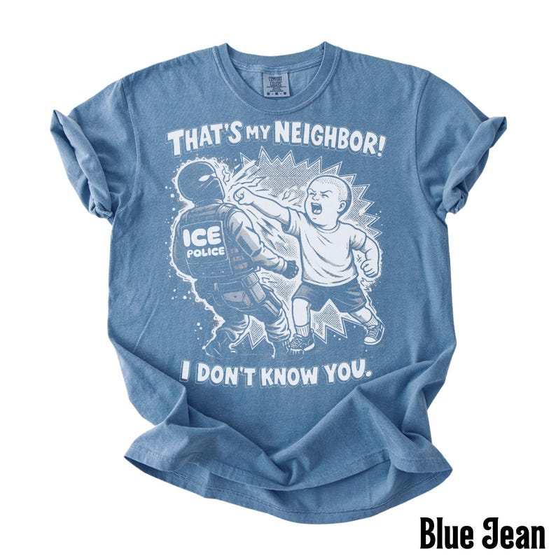 K&ouml;nnte beinhalten: Blaues Jeans-T-Shirt mit einer Grafik eines Kindes, das einen ICE-Polizisten schl&auml;gt. Der Text auf dem Shirt lautet: "THAT'S MY NEIGHBOR! I DON'T KNOW YOU."