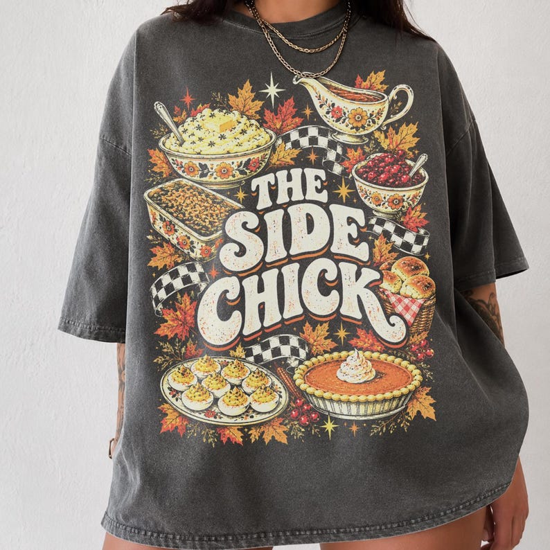 May include: A charcoal gray oversized t-shirt featuring a graphic print of various Thanksgiving side dishes, including mashed potatoes, gravy, stuffing, cranberry sauce, deviled eggs, and pumpkin pie, with the text THE SIDE CHICK.