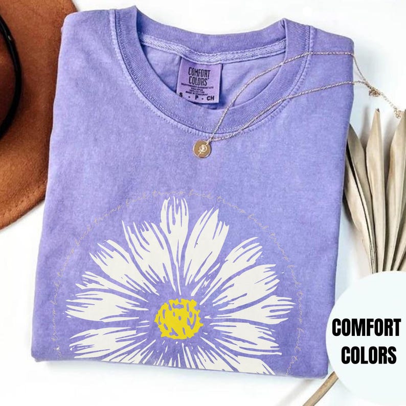 May include: Purple t-shirt with a white daisy graphic and the text "You are your own kind of beautiful" printed around the flower. The shirt is made by Comfort Colors.