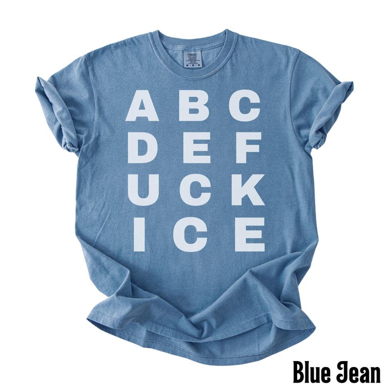 May include: A blue t-shirt with the word "DUCK" in large white capital letters, along with other letters arranged in a grid. The text "Blue Jean" is at the bottom right corner of the shirt.