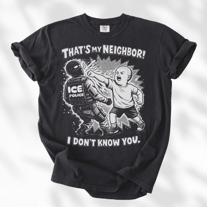K&ouml;nnte beinhalten: Schwarzes T-Shirt mit einer Grafik eines Babys, das einen ICE-Polizisten schl&auml;gt. Der Text auf dem Shirt lautet: "THAT'S MY NEIGHBOR! I DON'T KNOW YOU."