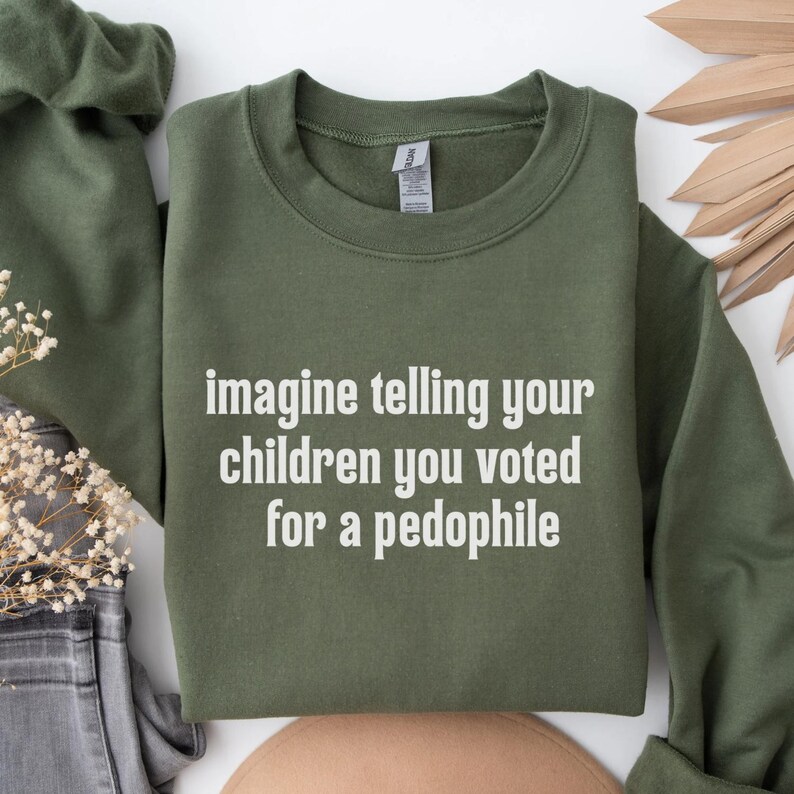 May include: An olive green sweatshirt with the text "imagine telling your children you voted for a pedophile" in white block letters. The sweatshirt is made of a soft material.