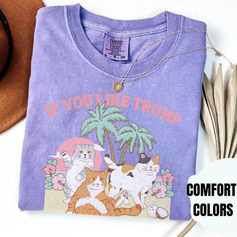 May include: Purple t-shirt with a graphic of three cats on a beach with palm trees and the text "If you like Trump". The shirt also has the text "Comfort Colors" on the bottom right corner.