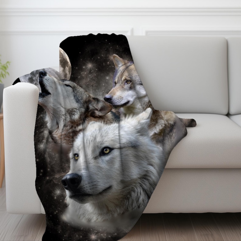 May include: A plush throw blanket featuring a striking image of wolves. The design showcases three wolves against a backdrop of a starry night and a full moon. The wolves are depicted in shades of gray, white, and brown.
