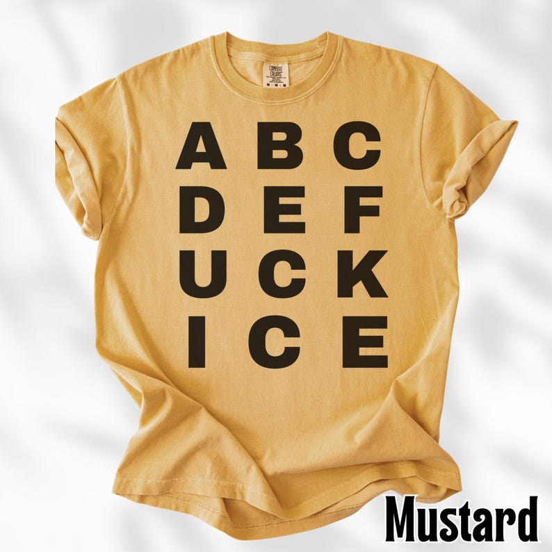 May include: Mustard-colored t-shirt with the word "Mustard" in a black font at the bottom right. The shirt features the letters "ABC DEF UCK ICE" in a black, bold font.