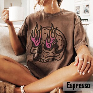 May include: Espresso-colored t-shirt featuring a skull graphic with flames in shades of pink and yellow. The shirt is a relaxed fit and has short sleeves. The word "Espresso" is printed at the bottom of the image.