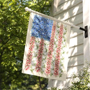 May include: A decorative garden flag featuring a floral American flag design. The flag's field is composed of blue flowers, while the stripes are made of red and white flowers. The flag is hanging on a white pole attached to a white house.
