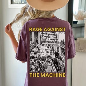 Puede incluir: Una camiseta malva con el texto "RAGE AGAINST THE MACHINE" en amarillo. La parte trasera de la camiseta presenta un gr&aacute;fico en blanco y negro de una protesta con las palabras "Undocumented People Feed Everyone, Billionaires Feed Themselves."