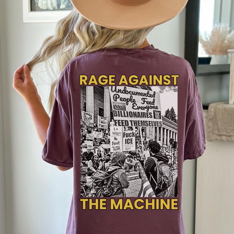 Puede incluir: Una camiseta malva con el texto "RAGE AGAINST THE MACHINE" en amarillo. La parte trasera de la camiseta presenta un gr&aacute;fico en blanco y negro de una protesta con las palabras "Undocumented People Feed Everyone, Billionaires Feed Themselves."