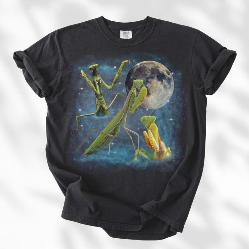 Puede incluir: Camiseta negra con un dise&ntilde;o gr&aacute;fico de tres mantis religiosas, una luna llena y un cielo estrellado. Las mantis est&aacute;n representadas en tonos verdes y amarillos. La camiseta est&aacute; hecha de un material suave y c&oacute;modo.