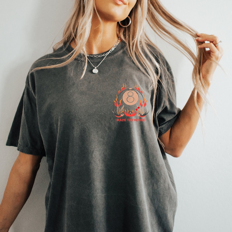 May include: A dark gray oversized t-shirt with a graphic of a pool ball on fire with the text "Made to Endure".