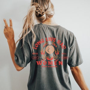 May include: A dark gray t-shirt with a graphic print of a red and orange eight ball with flames and the text "Long Live Rad Women" in red and orange. The text "Raise Est 1994 Hell" is printed in a circle around the eight ball.
