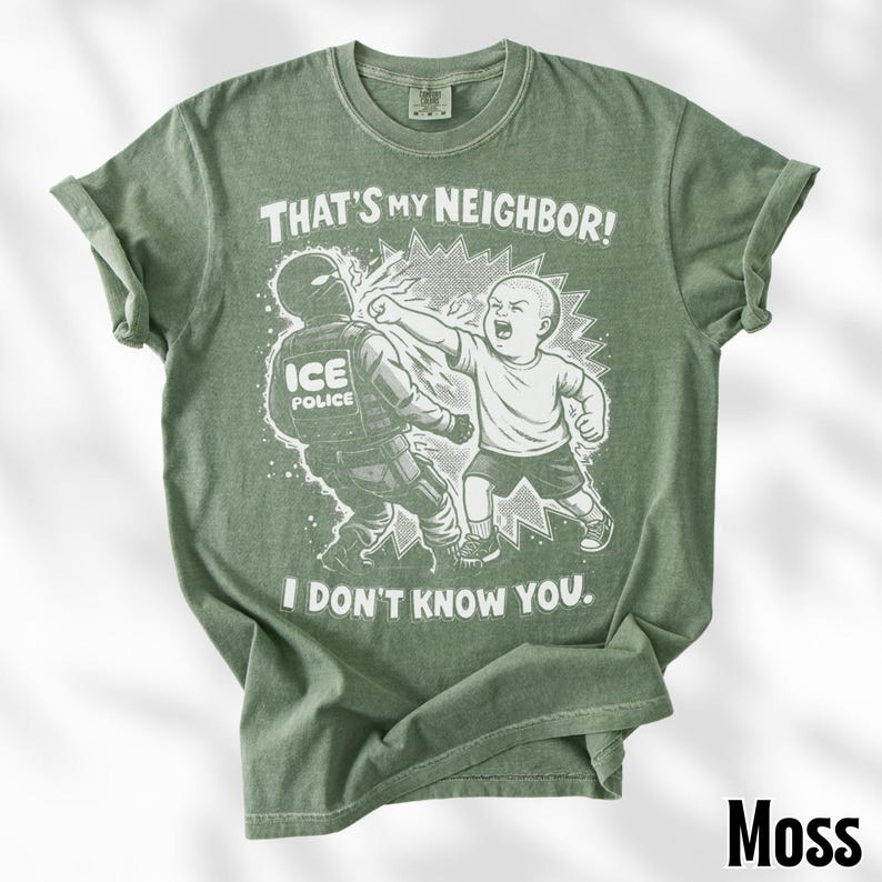 K&ouml;nnte beinhalten: Moosgr&uuml;nes T-Shirt mit einer grafischen Illustration eines Kindes, das einen ICE-Polizisten schl&auml;gt. Der Text auf dem Shirt lautet: "THAT'S MY NEIGHBOR! I DON'T KNOW YOU."
