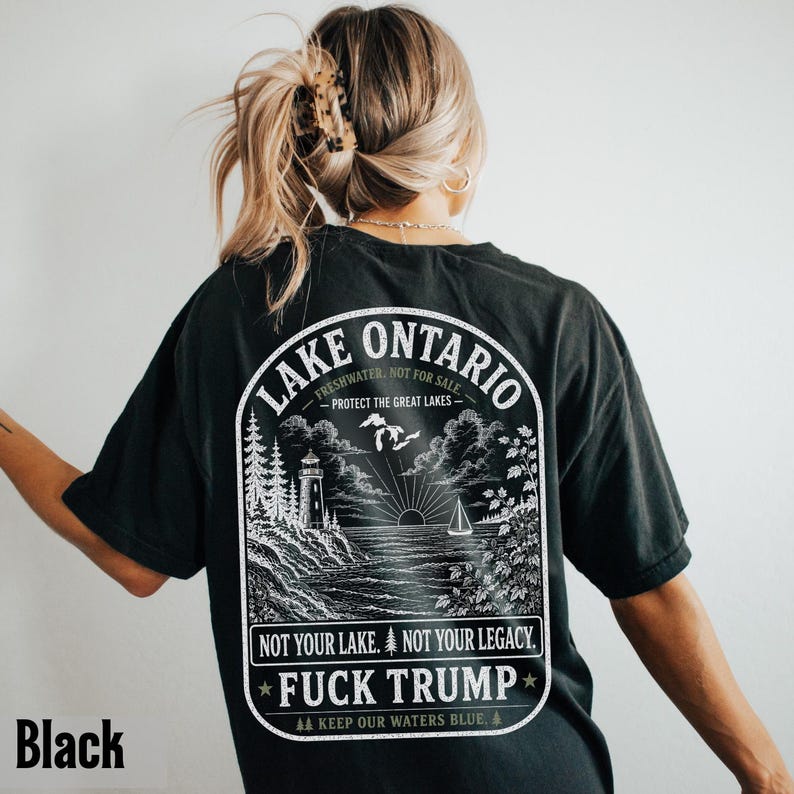 May include: A black t-shirt featuring a white graphic on the back. The design depicts a lighthouse, a sailboat, and a lake landscape with the text: LAKE ONTARIO, FRESHWATER, NOT FOR SALE, PROTECT THE GREAT LAKES, NOT YOUR LAKE. NOT YOUR LEGACY. FUCK TRUMP.