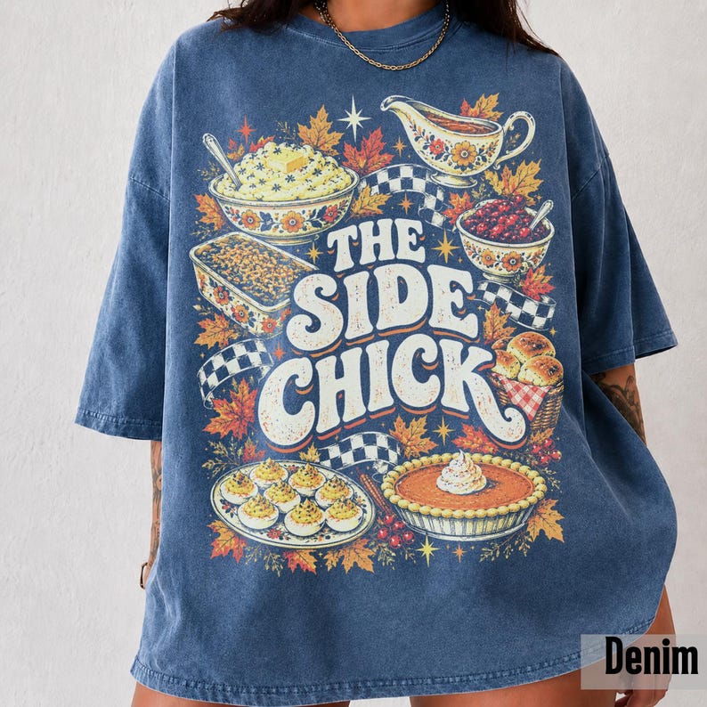 May include: A blue acid-wash t-shirt featuring a graphic print of Thanksgiving side dishes including mashed potatoes, gravy, stuffing, cranberry sauce, deviled eggs, and pumpkin pie, with the text THE SIDE CHICK in large white letters.