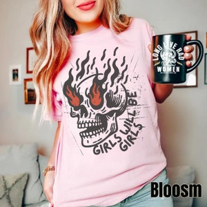 May include: Pink t-shirt featuring a graphic of a skull with flames for eyes and the text "Girls will be girls".