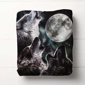 May include: A black blanket featuring a nighttime scene with three wolves howling at a full moon. The wolves are depicted in shades of gray and black, with the moon in a bright white color. The background has a starry night sky.