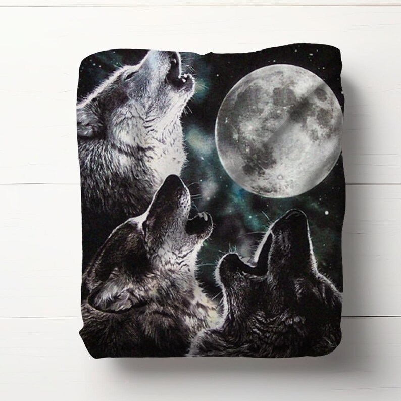 May include: A black blanket featuring a nighttime scene with three wolves howling at a full moon. The wolves are depicted in shades of gray and black, with the moon in a bright white color. The background has a starry night sky.