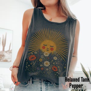 Puede incluir: Camiseta sin mangas gris oscuro con un dise&ntilde;o de sol y flores. El sol tiene los ojos cerrados y mejillas rosadas, con una explosi&oacute;n amarilla. Las flores incluyen margaritas y amapolas. El texto "Relaxed Tank Pepper" est&aacute; en la parte inferior.
