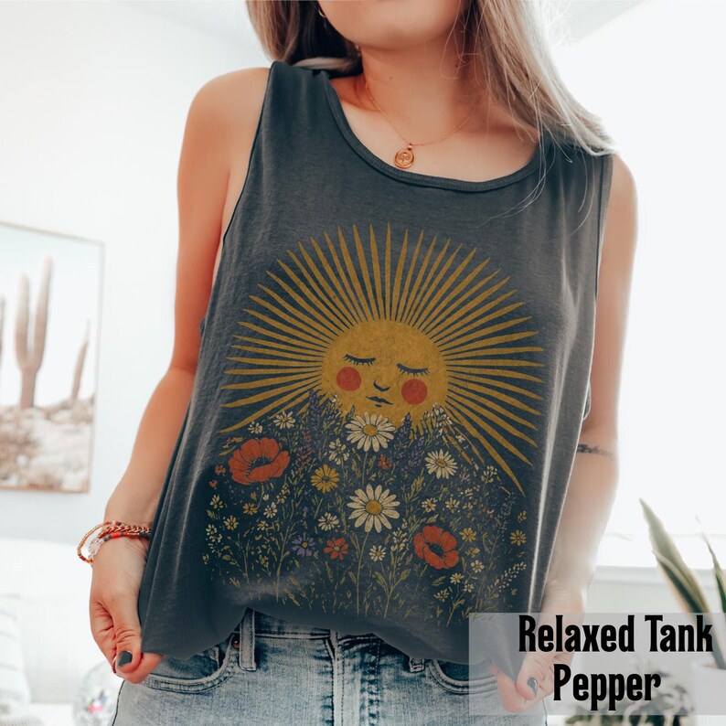 Puede incluir: Camiseta sin mangas gris oscuro con un dise&ntilde;o de sol y flores. El sol tiene los ojos cerrados y mejillas rosadas, con una explosi&oacute;n amarilla. Las flores incluyen margaritas y amapolas. El texto "Relaxed Tank Pepper" est&aacute; en la parte inferior.