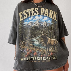 May include: Dark gray t-shirt featuring a scenic illustration of Estes Park, Colorado. The design includes a mountain range, river, elk, and the text "ESTES PARK" and "WHERE THE ELK ROAM FREE - COLORADO ROCKIES".